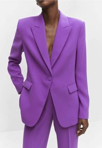 Blazer morado a medida con solapas afiladas, cierre de un solo botón y dos bolsillos, confeccionado con tela texturizada. Diseño minimalista.