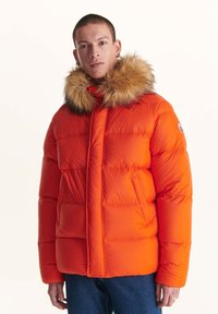 Oranje pufferjack met een met bont gevoerde capuchon, voorzien van een gequiltde structuur en een ritssluiting aan de voorkant. Dubbele zijzakken en een logo patch op de mouw.