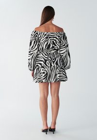 Sukienka w czarno-biały wzór zebry z odkrytymi ramionami, z długimi rękawami, elastyczną talią i warstwową spódnicą. Gładki, lekki materiał.