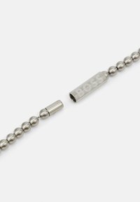 Metal necklace featuring a series of round metallic beads and a rectangular pendant engraved with "BOSS." Color: silver.