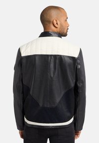 Sort læderjakke med en hvid kviltet skulderparti, struktureret detaljer på ryggen og en tætsiddende pasform. Stylet med mørke jeans.