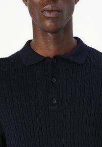 Marinblå kabelstickad polo t-shirt med ett texturerat mönster, treknappsknäppning och ribbad krage. Mjuk tyg med en figurnära design.