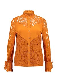 Blusa arancione con sovrapposizione di pizzo con motivi floreali, apertura frontale con bottoni, colletto alto e polsini a balze accentuati da bottoni.