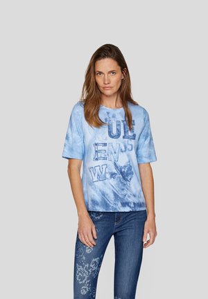 Hellblaues Baumwoll-T-Shirt mit kurzen Ärmeln, das große Grafikbuchstaben und Blumenmuster zeigt, kombiniert mit blauen Jeans.