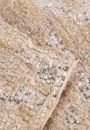 Beige paillettenstof met gestructureerde stroken, voorzien van zilveren, gouden en zwarte accenten, gelaagd met zacht, doorschijnend materiaal en delicate versieringen.