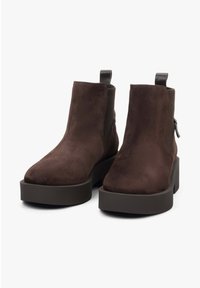 Bruine suede enkellaarsjes met een platte, stevige zool. Voorzien van elastische zijpanelen en een hiel lus voor gemakkelijk aan- en uittrekken. Minimalistisch ontwerp zonder versieringen.