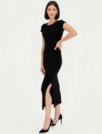 Czarna sukienka z prążkowanej tkaniny o dopasowanej sylwetce, krótkimi rękawami, bocznym rozcięciem i długości do kolan, zestawiona z czarnymi szpilkami w szpic.