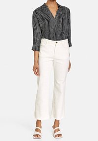 Blouse à rayures noirs et blancs avec un col, assortie à un pantalon blanc taille haute avec un motif texturé subtil et des ourlets effilochés.