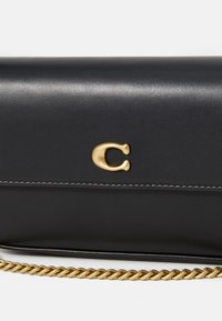 Black leather clutch with gold C logo on front flap and gold chain strap partially visible at bottom on white background.