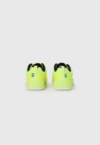 Neon gule sneakers med sort kant, udstyret med en trækflap og en tekstureret overflade. Hvid gummisål med branding på hælen.
