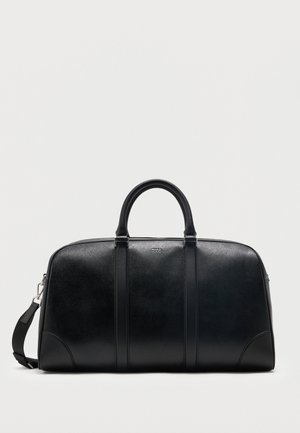 Bolsa de viaje de cuero negro con dos asas superiores, correa de hombro desmontable y pequeño logo "Hugo" centrado cerca de la cremallera superior.