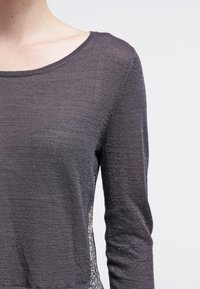 Dark gray long-sleeve top with a textured knit body, featuring a wide neckline and patterned side panels. Soft, lightweight fabric.