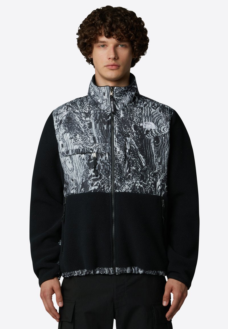 Polarowa kurtka o czarnej korpusie i teksturowanej, monochromatycznej wzorzystej klatce piersiowej. Posiada wysoki kołnierz, zamykane kieszenie oraz pełny zamek z przodu.