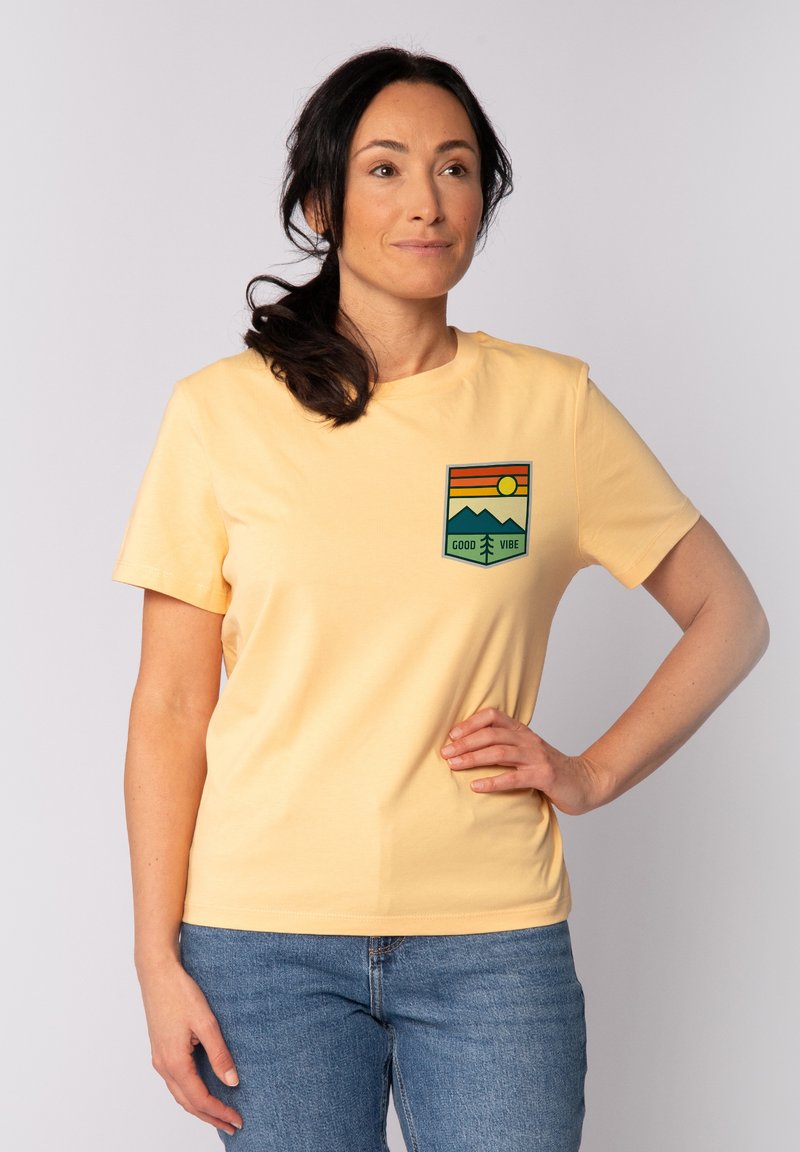 T-shirt en coton jaune à manches courtes avec un graphique coloré de montagne et de soleil sur le côté gauche de la poitrine. Coupe classique.
