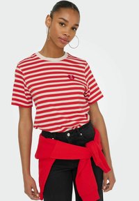 Rød- og hvidstribet t-shirt med korte ærmer, rund halsudskæring og et lille hjerte-logo. Bæres med sorte bukser og en rød trøje bundet om livet.