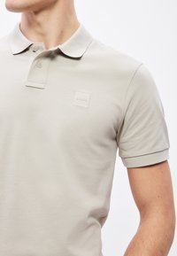 Ανοιχτό γκρι πόλο πουκάμισο με υφή, διαθέτει πατιλέτα με τρία κουμπιά και μικρό, τετράγωνο λογότυπο στο στήθος.