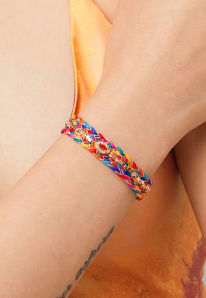 Bracelet tressé multicolore avec des accents dorés brillants, présenté dans des rouges, bleus et jaunes vifs, porté au poignet.