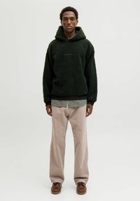 Ciemnozielona polarowa bluza z kapturem z kieszenią z przodu, nałożona na koszulę w kratę. W zestawie beżowe spodnie i brązowe buty.