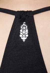 Top de fato de banho preto em tecido com decote franzido e um detalhe de logótipo floral branco. Textura suave com alças ajustáveis.