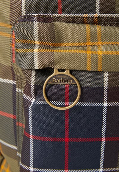 Gros plan sur une poche de veste Barbour avec un motif tartan multicolore et un bouton circulaire en laiton portant la marque.