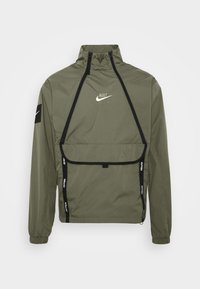Olivgrön Nike-jacka med hög krage, ficka fram och svarta accentfärger. Har långa ärmar och logotyp på bröstet och ärmen. Lätt material.