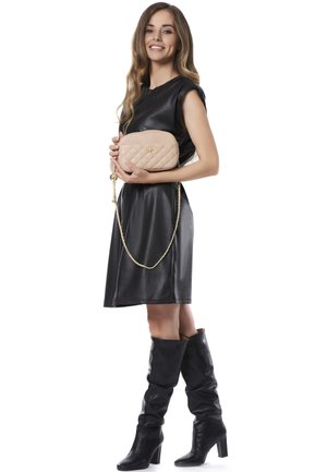 Abito di pelle nera, borsa beige trapuntata con tracolla a catena, stivali neri al ginocchio, design elegante, texture liscia.