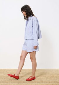 Blau-weiße gestreifte kurzärmlige Hemd und passende Shorts mit lockerem Schnitt. Rote Ballerinas. Hintergrund mit gewebter Textur.