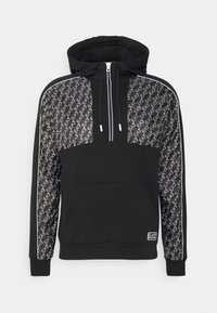 Svart huvtröja med framficka, har ett mönstrat panel på axlarna, kontrasterande ränder och en dragkedja. Mjuk tygtextur.