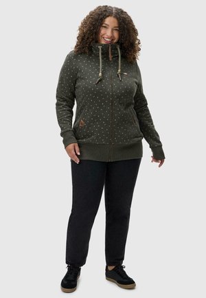 Dark green zip-up hoodie with a high collar, white dot pattern, and brown leather accents. Paired with black jeans and black shoes.