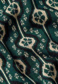 Grüner Strickstoff mit beigem Blumenmuster, schwarz umrandet. Strukturiert mit einem weichen Gewebe und sich wiederholenden geometrischen Formen.