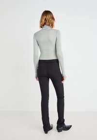 Lysegrønn langermet turtleneck-toppen kombinert med svarte tettsittende bukser. Toppen har en glatt, stretchy tekstur; buksene er stilige med en lett flare.