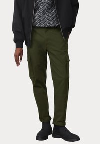 Cargo broek in donkergroen, met meerdere zijzakken, een relaxte pasvorm en omgeslagen broekspijpen, gecombineerd met een zwarte ritsjack.