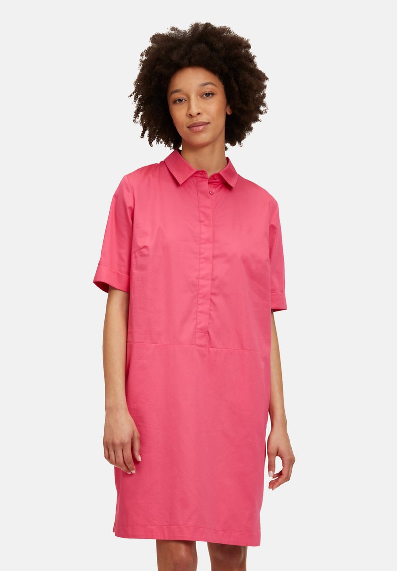 Kurzärmliges, kragenloses Kleid aus leuchtend pinkem Stoff. Verfügt über eine Knopfleiste und einen lockeren Schnitt, mit einer glatten Textur und einer Länge bis zur Mitte des Oberschenkels.