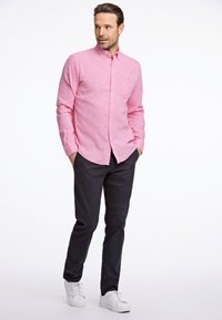 Vaaleanpunainen pitkähihaisten nappikauluspaita, jossa on tasku, yhdistetty tummiin housuihin ja valkoisiin lenkkareihin. Paita on rento ja siinä on teksturoitu kangas.