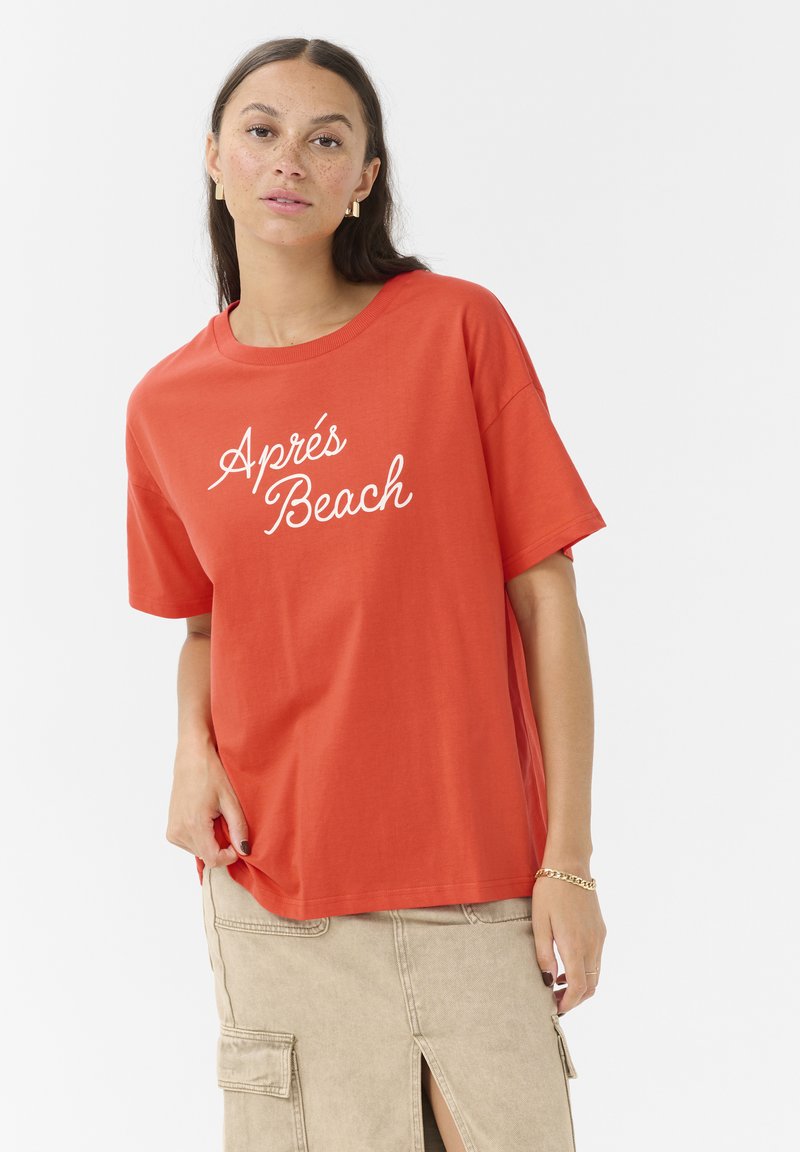 Rød bomulds t-shirt med korte ærmer og rund hals. Har hvid kursiv tekst "Après Beach" på forsiden. Casual fit og blød tekstur.