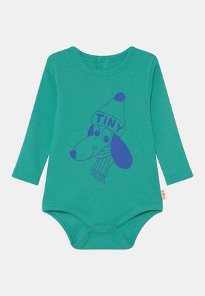 Turkusowy bodysuit z długim rękawem, z prążkowanej tkaniny. Posiada niebieskiego psa z kreskówki noszącego kapelusz z napisem "TINY" oraz szalik, z zapięciami na napy u dołu.