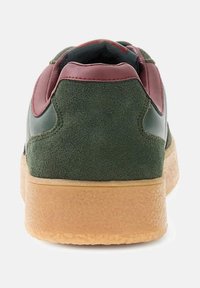 Sneaker widziany z tyłu, z zielonym zamszem, bordowymi skórzanymi wykończeniami, czarnym wnętrzem i teksturowaną jasnobrązową podeszwą.