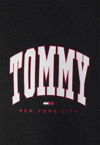 Sudadera negra con el texto en negrita blanco "TOMMY" arqueándose sobre "NEW YORK CITY" en rojo. Incluye un pequeño acento en rojo, blanco y azul.