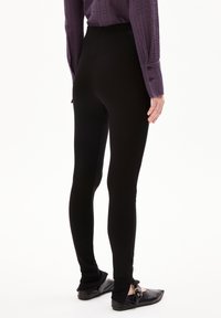 Zwarte leggings gemaakt van rekbaar materiaal, aansluitend design, hoge taille, gladde textuur en met een subtiele naaddetail bij de enkel.