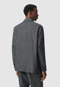 Camicia grigia in tessuto intrecciato con colletto, maniche lunghe e polsini con bottone. La vista posteriore mostra un taglio dritto e una texture sottile. Nessun motivo o accento.