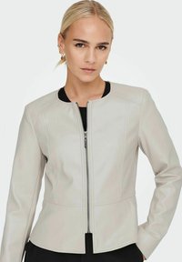 Jachetă din faux leather de culoare gri deschis, cu guler rotund și fermoar pe față. Prezintă detalii cu cusături și o siluetă ajustată.