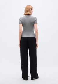 Γκρι εφαρμοστό τοπ με κοντά μανίκια, συνδυασμένο με μαύρο ψηλόμεσο παντελόνι φαρδιάς γραμμής, με ανάγλυφη υφή ριμπ και λείο φινίρισμα υφάσματος.