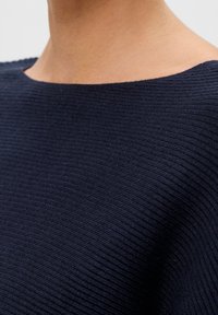 Světle modrý žebrovaný pletený svetr s širokým výstřihem a texturovaným povrchem, s rovnoměrně hladkým finálním vzhledem na látce.