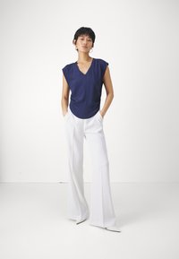 Maglietta blu navy a scollo a V con maniche corte abbinata a pantaloni bianchi a gamba larga, che mette in risalto un tessuto morbido e una vestibilità rilassata.
