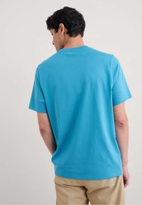 Trumpo rankovėmis, apvaliu kaklu, ryškiai mėlynas medvilninis marškinėlis. Lygus paviršius su laisvu priderinimu, rodomas iš nugaros. Be raštų ar grafikos.