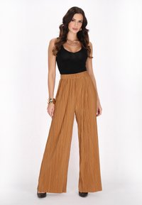 Braune, plissierte weite Hosen mit elastischem Bund, kombiniert mit einem figurschmeichelnden schwarzen Tanktop. Schwarze, mit Nieten besetzte High Heels runden den Look ab.