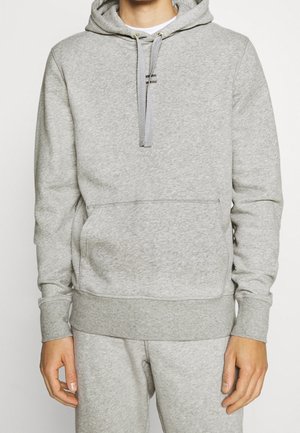 Person trägt einen hellgrauen Kapuzenpullover mit Kängurutasche und passende graue Jogginghose.