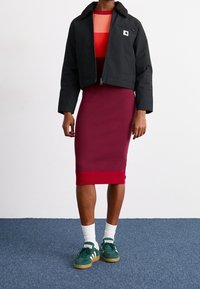 Zwart cropped jack met een harige kraag, rode geribbelde jurk met een lagere rode band, witte sokken, groene sneakers met bruine zolen.