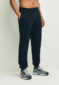 Dunkelblaue Jogginghosen mit elastischem Bund, zwei Seitentaschen und engen Bündchen. Kombiniert mit schwarzen und grauen Sportschuhen.