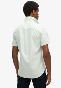 Camicia a maniche corte verde chiaro con colletto pieghevole, spacco posteriore dritto e orlo arrotondato. Realizzata in un morbido misto cotone.